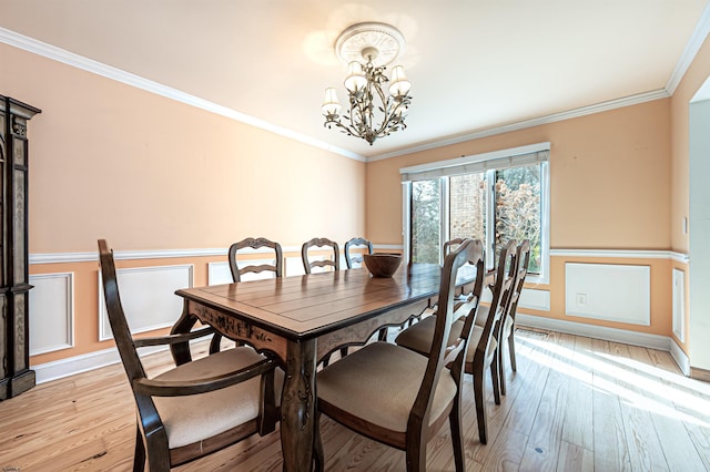 dining space featuring light wood-type flooring, an inviting chandelier, ornamental molding, and a wainscoted wall