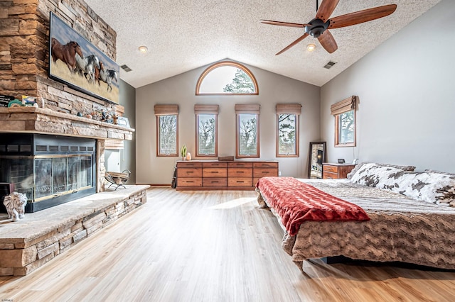 bedroom featuring visible vents, lofted ceiling, wood finished floors, a textured ceiling, and a stone fireplace