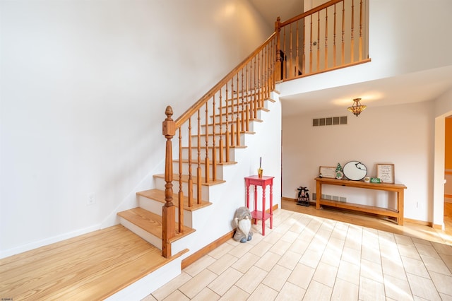 staircase featuring a towering ceiling, baseboards, visible vents, and wood finished floors