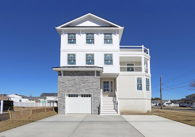 view of front of house featuring concrete driveway, a balcony, stone siding, metal roof, and a standing seam roof