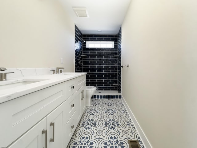 bathroom with baseboards, tiled shower, toilet, tile patterned flooring, and a sink