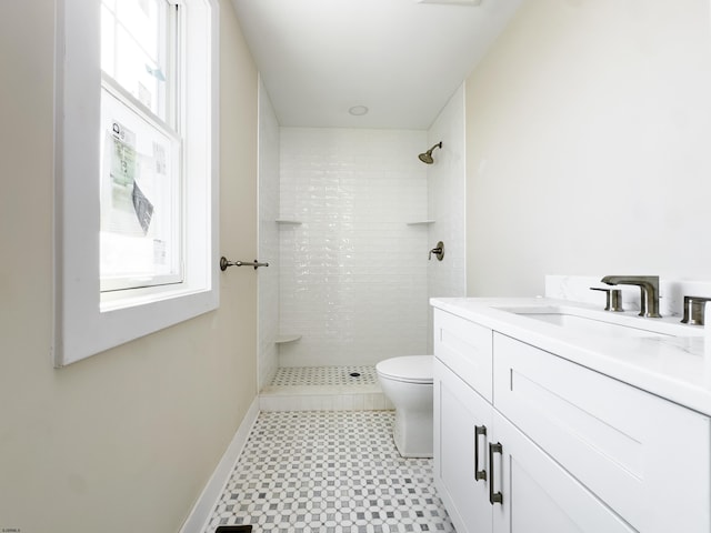 bathroom with toilet, baseboards, a tile shower, and vanity