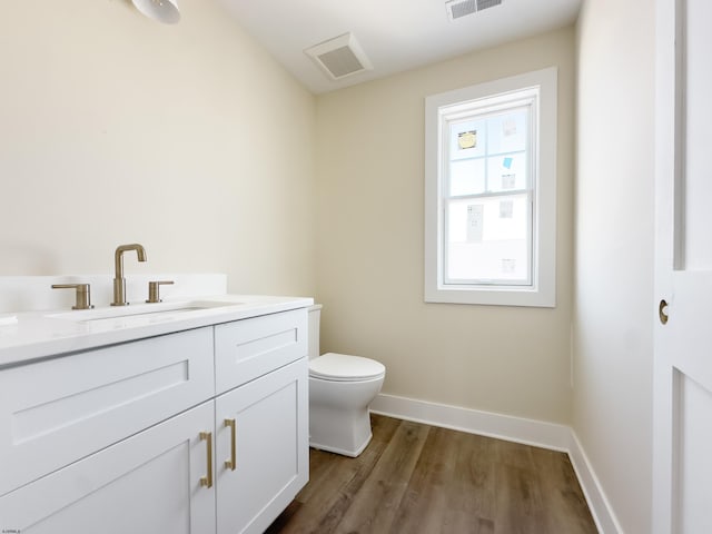 half bath featuring visible vents, baseboards, toilet, wood finished floors, and vanity