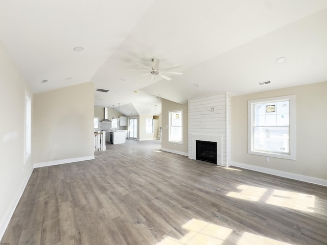 unfurnished living room featuring lofted ceiling, ceiling fan, a fireplace, wood finished floors, and visible vents