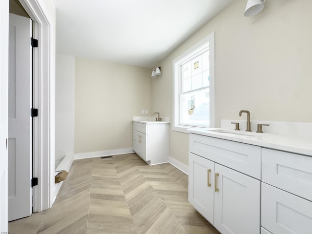 full bath featuring two vanities, a sink, and baseboards