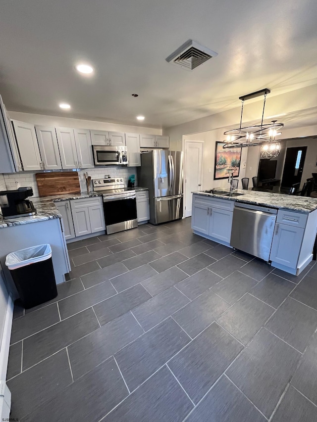 kitchen with a sink, visible vents, appliances with stainless steel finishes, backsplash, and pendant lighting