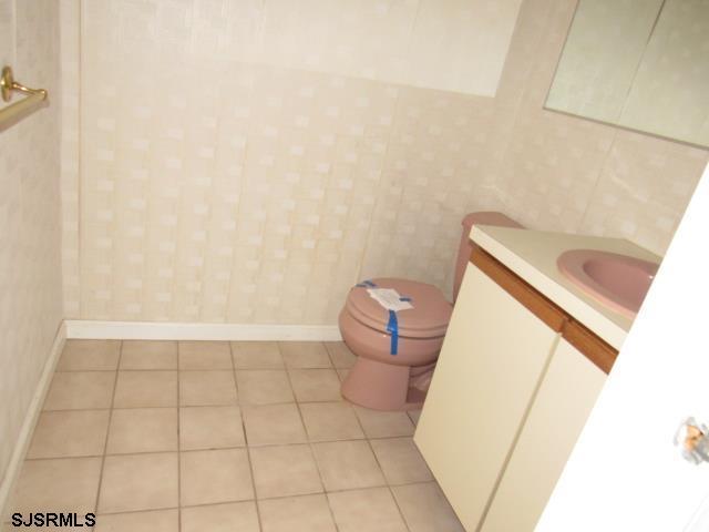 half bathroom with toilet, tile patterned flooring, vanity, and baseboards