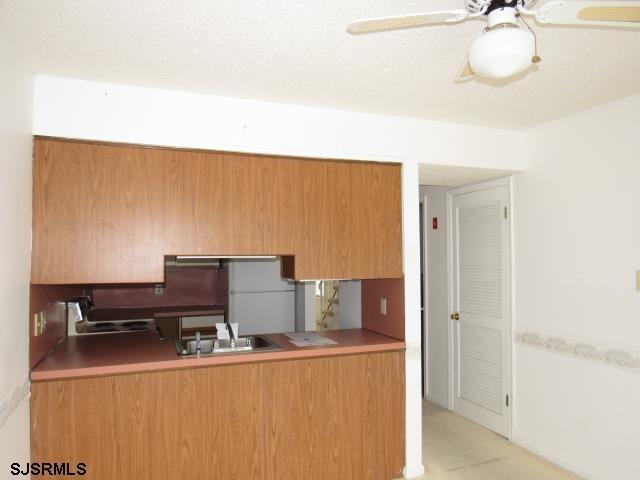 kitchen featuring a ceiling fan, freestanding refrigerator, brown cabinetry, and stovetop