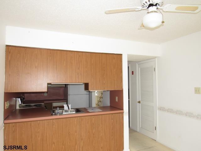 kitchen with ceiling fan, brown cabinetry, a sink, and freestanding refrigerator