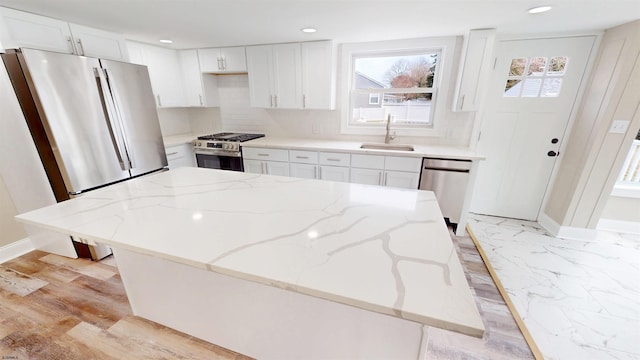 kitchen featuring decorative backsplash, appliances with stainless steel finishes, light stone countertops, white cabinetry, and a sink