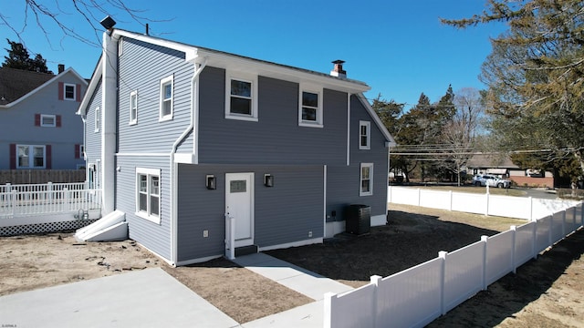 rear view of property with a wooden deck, a fenced backyard, cooling unit, and a chimney