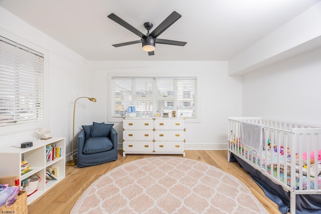 bedroom featuring a crib, ceiling fan, baseboards, and wood finished floors