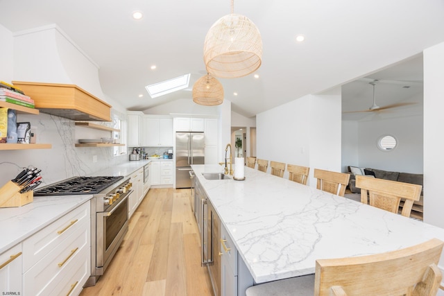 kitchen featuring light wood finished floors, lofted ceiling with skylight, a sink, high quality appliances, and a large island with sink