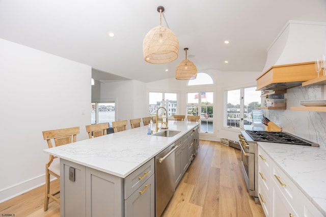 kitchen with gray cabinetry, stainless steel appliances, a sink, open shelves, and a kitchen bar