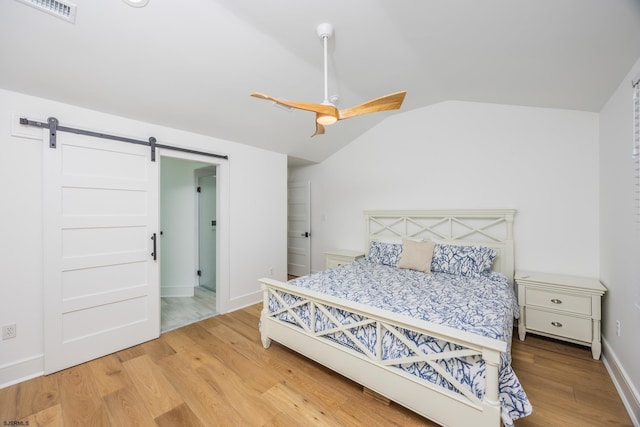 bedroom featuring light wood finished floors, lofted ceiling, visible vents, a barn door, and ceiling fan