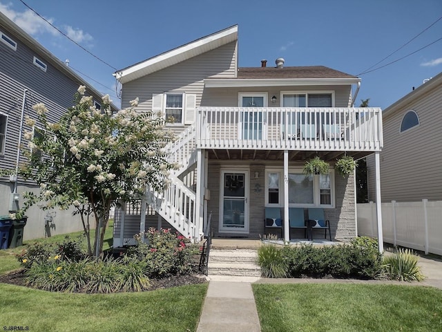 view of front of house with covered porch, fence, stairway, and a front lawn