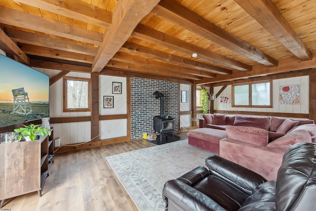 living area featuring a wood stove, plenty of natural light, beam ceiling, and wood finished floors