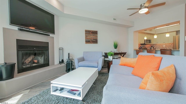 living room with a fireplace with raised hearth, ceiling fan, and light wood-style flooring