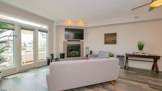 living area featuring a fireplace with raised hearth, ceiling fan, visible vents, and wood finished floors