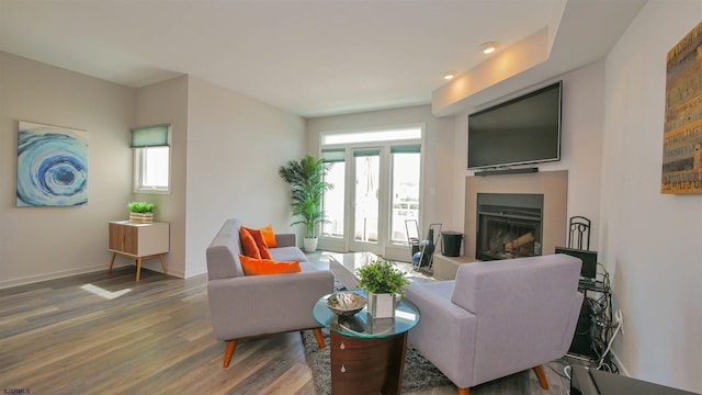 living area featuring a fireplace with raised hearth, wood finished floors, and baseboards