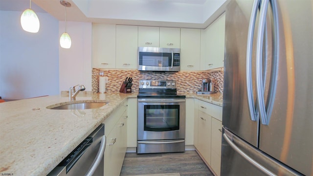 kitchen with light stone counters, stainless steel appliances, a sink, backsplash, and dark wood-style floors