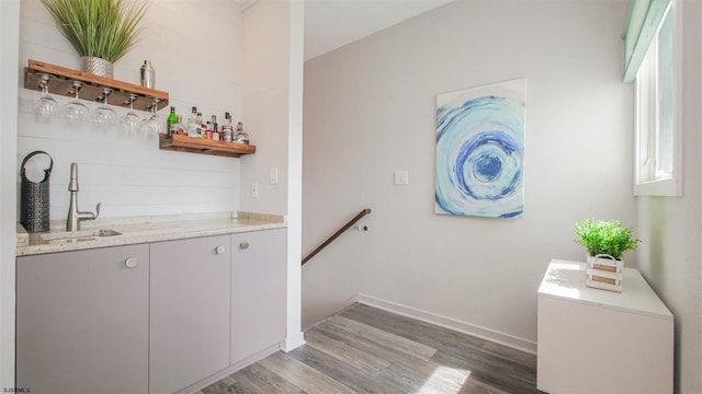 bar with wet bar, baseboards, a sink, and wood finished floors