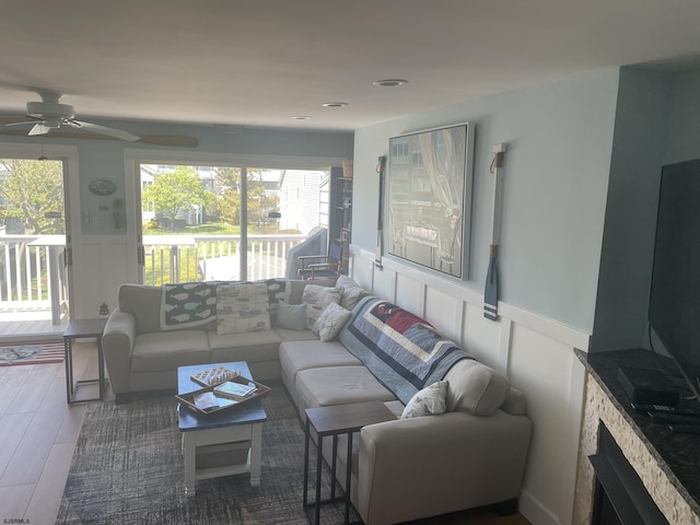 living area featuring a ceiling fan, wainscoting, a decorative wall, and wood finished floors