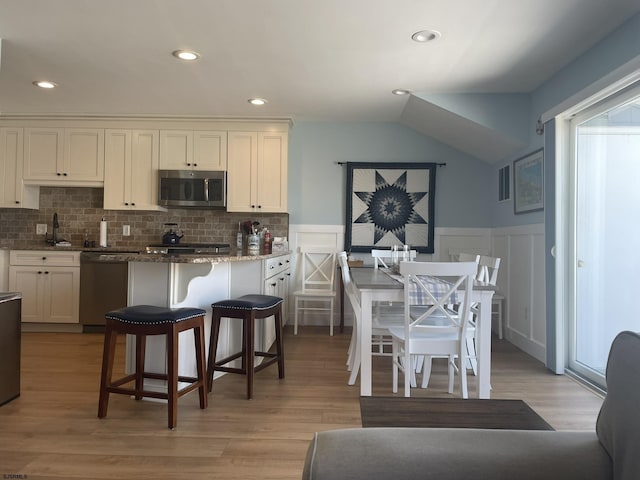 kitchen with a wainscoted wall, light wood-style flooring, appliances with stainless steel finishes, and backsplash