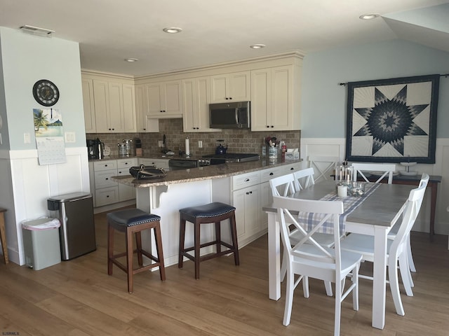 kitchen with light wood-type flooring, a wainscoted wall, a kitchen bar, and stainless steel microwave