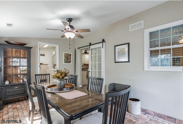 dining room featuring brick floor, a barn door, visible vents, and ceiling fan