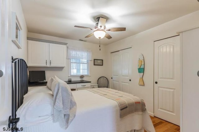 bedroom with ceiling fan, light wood finished floors, visible vents, and multiple closets