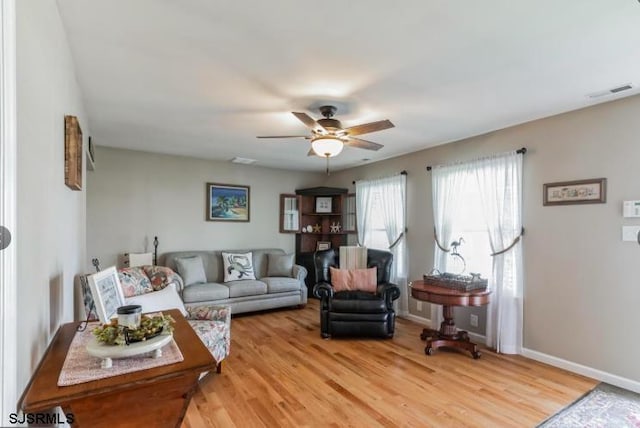 living area with a ceiling fan, baseboards, visible vents, and light wood finished floors