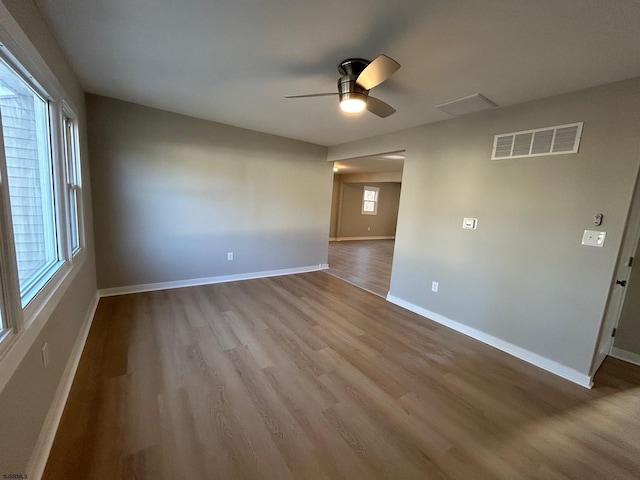 empty room with a ceiling fan, wood finished floors, visible vents, and baseboards