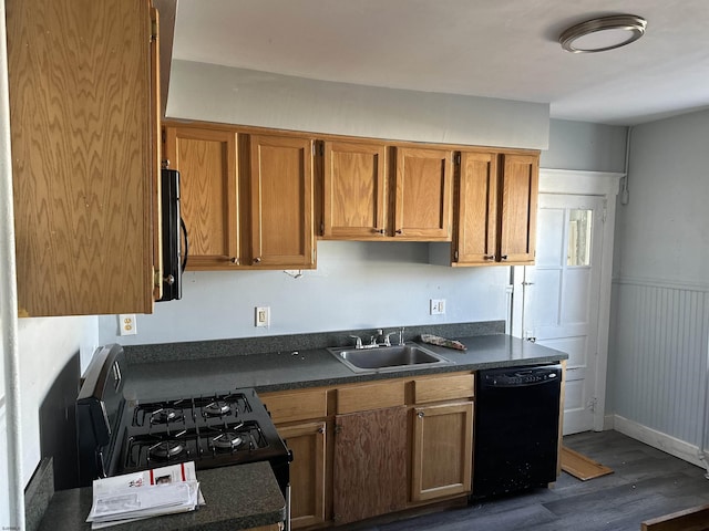 kitchen with a wainscoted wall, dark wood-style flooring, a sink, black appliances, and dark countertops