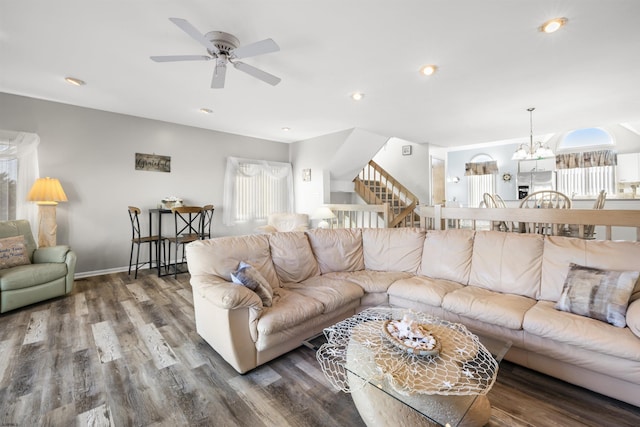 living area with recessed lighting, ceiling fan with notable chandelier, wood finished floors, baseboards, and stairs