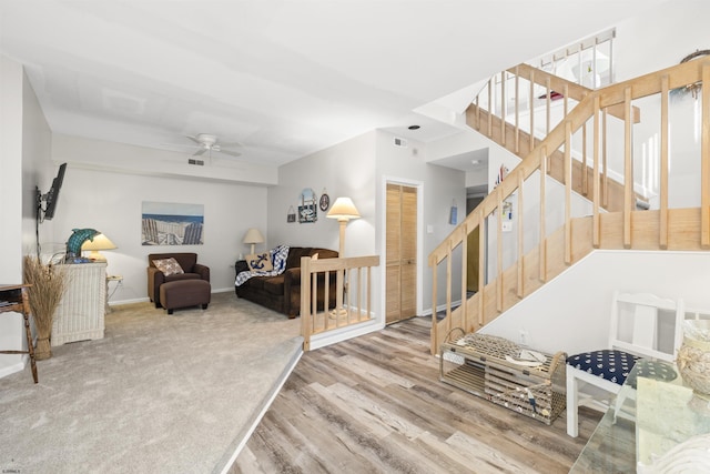 carpeted living area featuring wood finished floors, ceiling fan, baseboards, and stairs