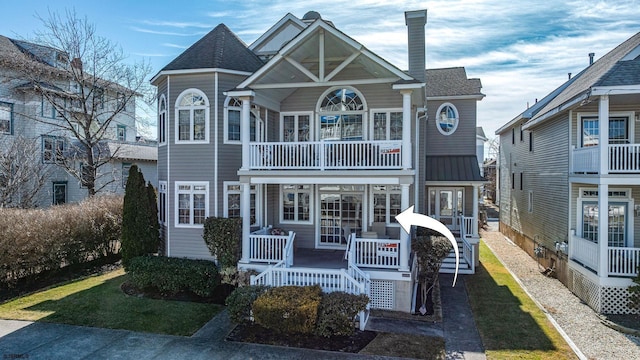 view of front of home featuring a porch, roof with shingles, a chimney, and a balcony