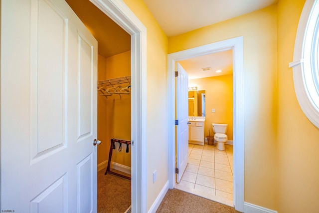 hallway with light tile patterned flooring, visible vents, and baseboards