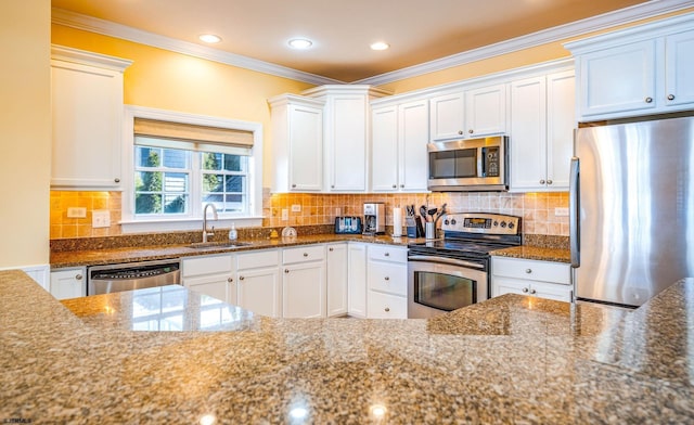 kitchen featuring white cabinets, appliances with stainless steel finishes, ornamental molding, dark stone countertops, and a sink