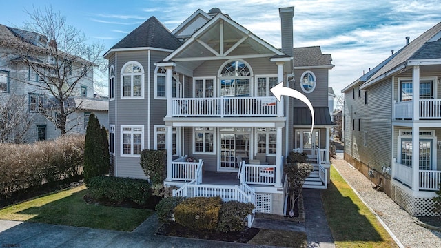 view of front of home with a balcony, covered porch, a shingled roof, and a chimney