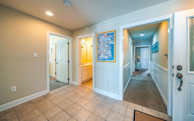 hall with light tile patterned floors, light carpet, attic access, and baseboards