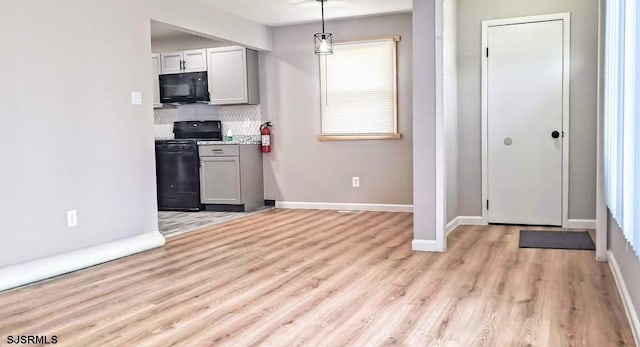 kitchen with black microwave, light wood-style flooring, baseboards, decorative backsplash, and gas range oven