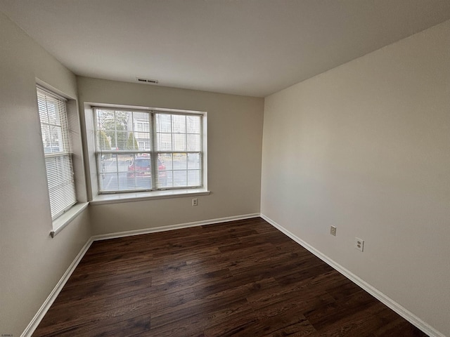 unfurnished room featuring dark wood finished floors, visible vents, and baseboards