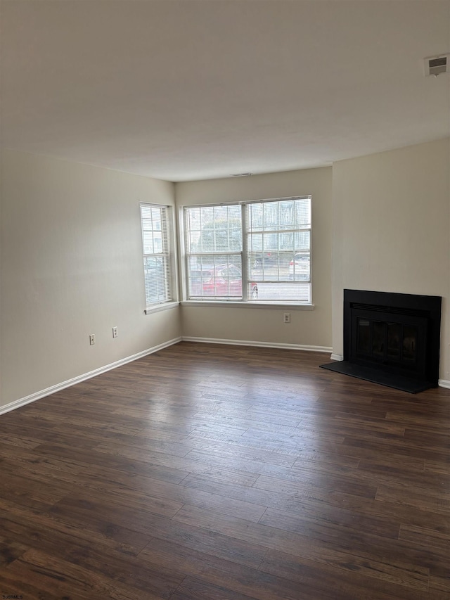 unfurnished living room with dark wood-style floors, a fireplace with raised hearth, visible vents, and baseboards