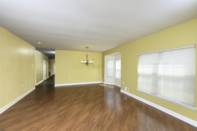 empty room featuring dark wood-style flooring, visible vents, baseboards, and an inviting chandelier