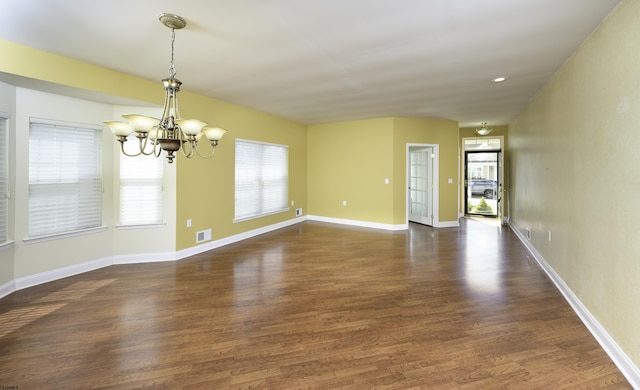 empty room featuring baseboards, visible vents, an inviting chandelier, and wood finished floors