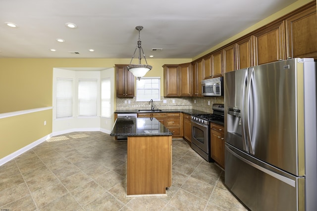 kitchen with a kitchen island, baseboards, hanging light fixtures, appliances with stainless steel finishes, and decorative backsplash