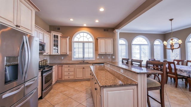 kitchen with a sink, a kitchen breakfast bar, appliances with stainless steel finishes, backsplash, and an inviting chandelier