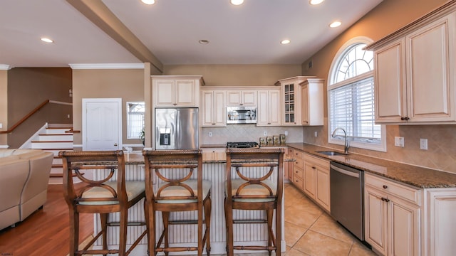 kitchen featuring appliances with stainless steel finishes, dark stone countertops, a center island, a kitchen bar, and a sink