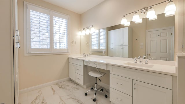 full bath featuring marble finish floor, double vanity, a sink, and baseboards